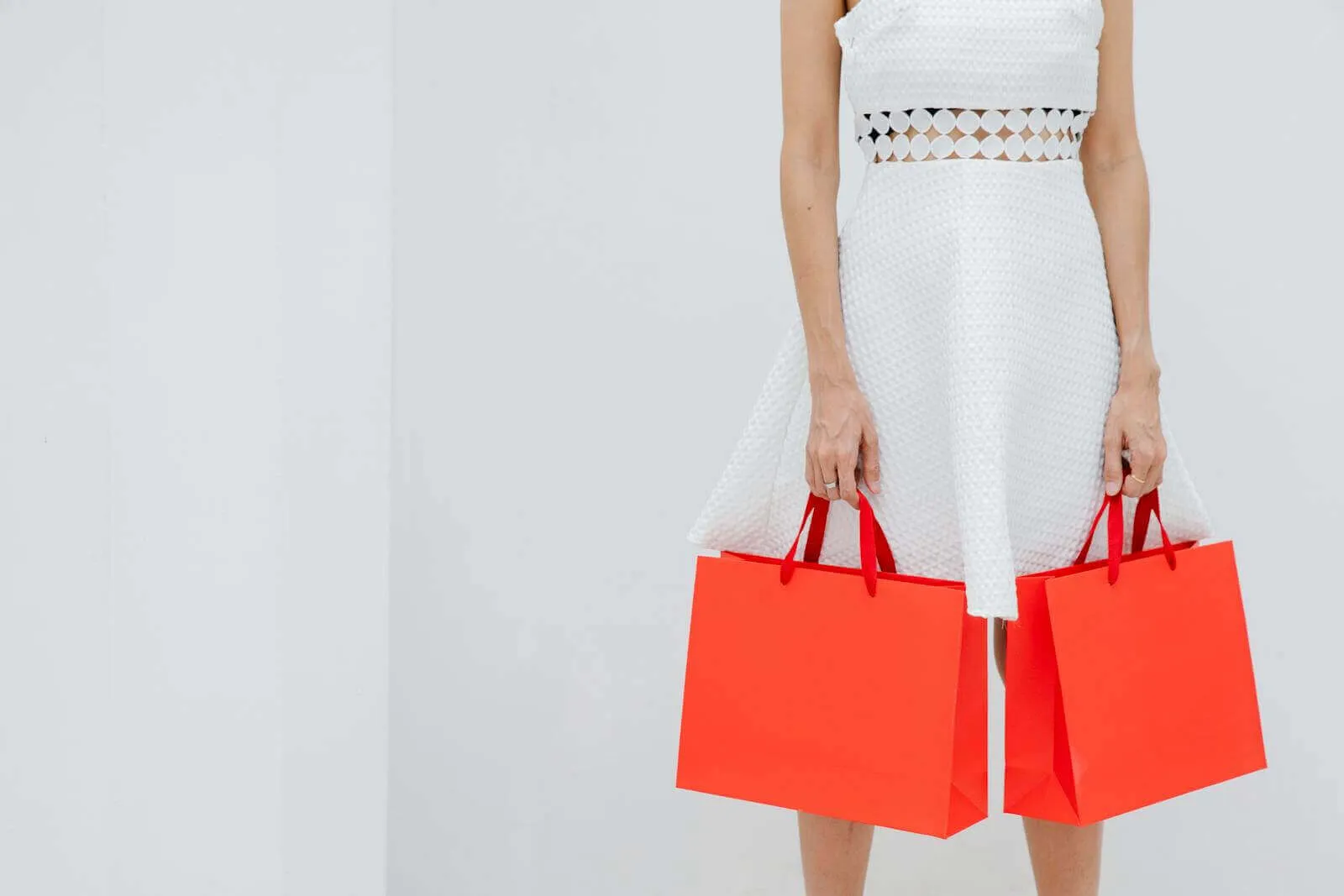 Crop unrecognizable woman carrying red shopping bags in studio